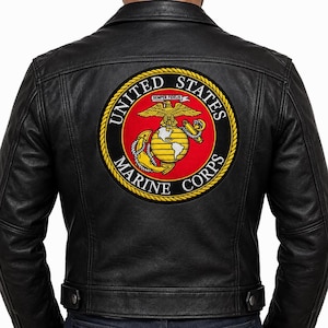 May include: A black leather jacket featuring a large, circular United States Marine Corps emblem embroidered on the back. The patch displays a gold eagle, globe, and anchor on a red background, surrounded by a yellow rope border and black text.