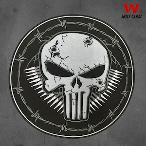 May include: A circular patch featuring a skull design with bullet holes and cracks, surrounded by barbed wire. The skull is white and gray, set against a black background. The text "WOLF CLAW" is in the upper right corner.