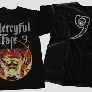 Może przedstawiać: Czarna koszulka z nazwą zespołu "Mercyful Fate - 9" w srebrnych gotyckich literach. Grafika z przodu zawiera czaszkę i płomienie. Tył przedstawia srebrne logo "9" z czaszką. Klasyczny t-shirt rock and roll.