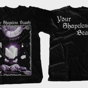 May include: Black t-shirt with a graphic print of a clock and a figure lying down. The text "Your Shapeless Beauty" is printed on the front of the shirt. The same text is printed on the back of the shirt.