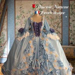 May include: A light blue gown with a large skirt and a fitted bodice. The gown is decorated with delicate floral embroidery and lace trim. The gown is styled in a French rococo design. The text "Rose raie Nocturne French design" is written above the gown.