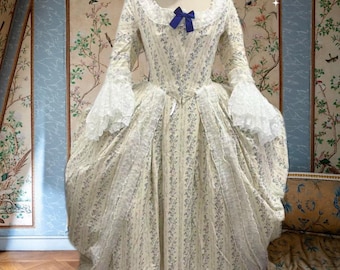 May include: A cream-colored, long-sleeved gown with a floral pattern and lace trim. The dress features a square neckline, a blue bow, and ruffled sleeves. The text "Roseraie Nocturne" is visible.