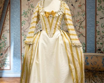 May include: A floor-length gown featuring a bodice and sleeves with yellow and white vertical stripes and floral patterns, a ruffled neckline, a small yellow bow at the center, and a solid cream-colored skirt. The text Roseraie Nocturne is visible.