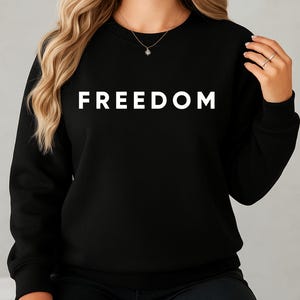 May include: Black sweatshirt with the word "FREEDOM" printed in large, white capital letters across the chest. The sweatshirt is a crew neck style and appears to be made of a soft material.