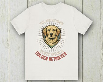 May include: White t-shirt featuring a Golden Retriever illustration within a shield design. The text reads "Feel Safe At Night Sleep With A Golden Retriever" in a circular layout. The design is in shades of gold, brown, and green.