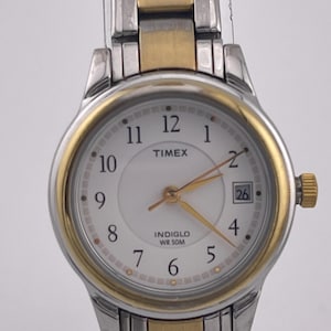 May include: A Timex watch with a white face, gold-tone bezel, and silver and gold-tone band. The watch face displays the time with black numerals and gold hands. The watch also has a date display at the 3 o'clock position.