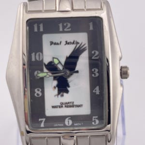 May include: A rectangular silver-toned wristwatch with a black face. The watch face features the text "Paul Jardin" and an eagle graphic. The watch also has the text "QUARTZ WATER RESISTANT" and "JAPAN MOVT".