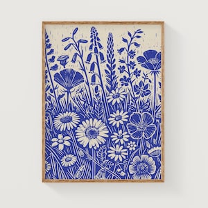 May include: A blue and white linocut print of a variety of flowers in a field. The print is framed in a natural wood frame.