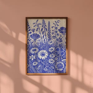May include: A framed print of a blue and white floral design. The print features a variety of flowers and leaves, including daisies, poppies, and bellflowers. The background is a light cream color.