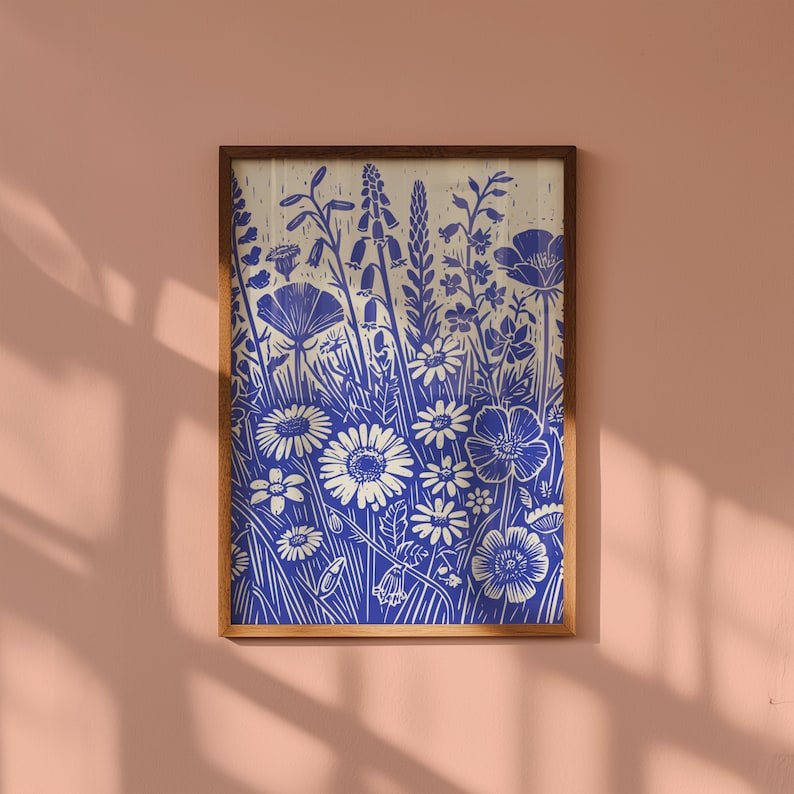 May include: A framed print of a blue and white floral design. The print features a variety of flowers and leaves, including daisies, poppies, and bellflowers. The background is a light cream color.