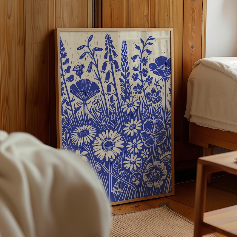 May include: A framed print of a blue and white floral design. The print features a variety of flowers, including daisies, poppies, and bellflowers. The flowers are arranged in a loose, organic pattern, and the background is a light cream color.