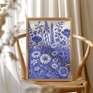 May include: A framed print of a blue and white floral design. The print features a variety of flowers and leaves, including daisies, poppies, and ferns. The background is a light cream color.