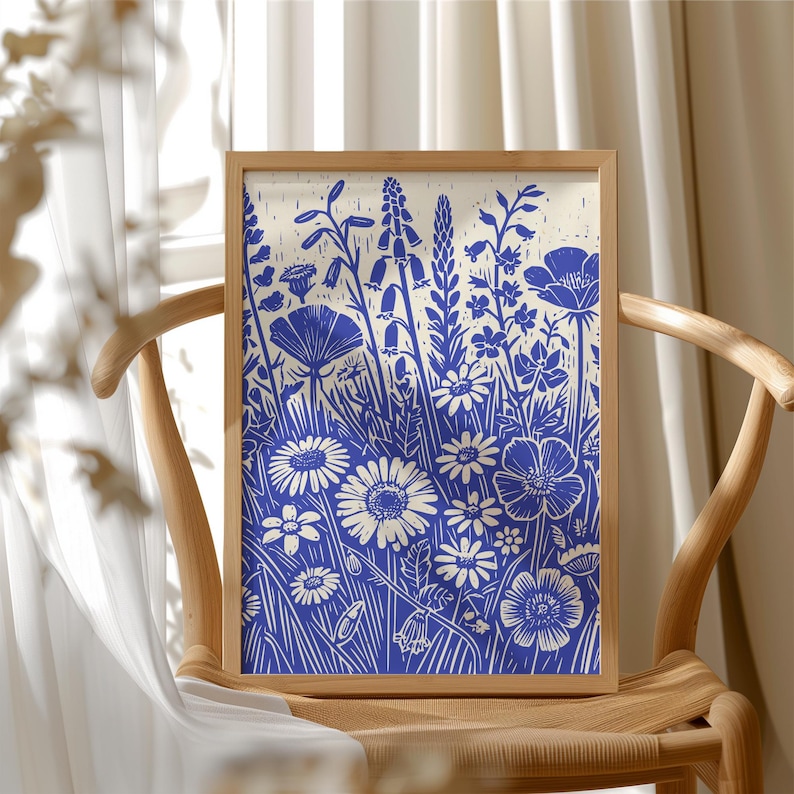 May include: A framed print of a blue and white floral design. The print features a variety of flowers and leaves, including daisies, poppies, and ferns. The background is a light cream color.