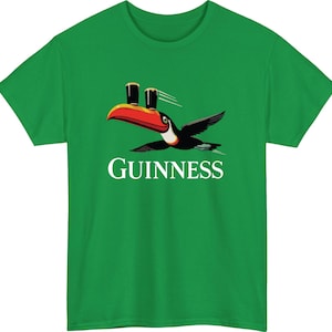May include: Green t-shirt featuring a toucan with a red beak and black wings, carrying two pints of dark beer. The word "GUINNESS" is printed in white below the bird. A fun and casual design.
