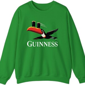 May include: Green sweatshirt featuring a toucan carrying two pints of Guinness. The toucan has a red and orange beak, black wings, and white accents. The word "GUINNESS" is printed in white below the toucan.