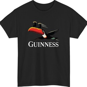 May include: Black t-shirt featuring a toucan with a red and orange beak, carrying two pints of stout. The word "GUINNESS" is printed in white below the bird. A classic design for fans of the Irish stout.