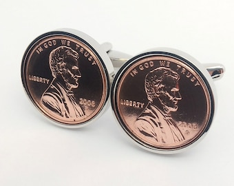 May include: A pair of cufflinks featuring a copper-colored penny with the image of Abraham Lincoln and the text "In God We Trust" and "Liberty". The year "2008" is also visible on the coin.