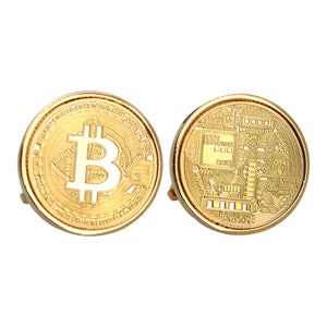 May include: A pair of gold-colored Bitcoin cufflinks. One cufflink features the Bitcoin symbol, while the other displays a circuit board design. The cufflinks have a shiny, metallic finish and a classic, round shape.