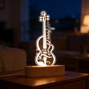 May include: A glowing violin-shaped night light with the name "Ashely" in a cursive font. The light sits on a rectangular wooden base and is connected to a power cord. The design includes a heartbeat line, suggesting a musical theme.