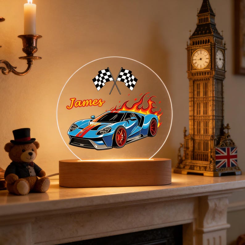 Puede incluir: L&aacute;mpara de noche decorativa con un dise&ntilde;o de coche deportivo azul con detalles rojos y llamas sobre un panel acr&iacute;lico redondo. El nombre "James" est&aacute; encima del coche, con dos banderas a cuadros. La base es de madera.