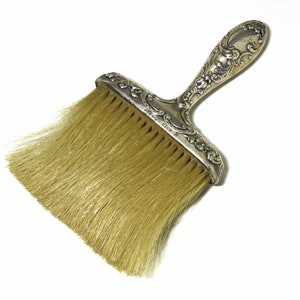 May include: A silver-plated brush with a decorative handle and natural bristles. The handle has an ornate design with a floral motif.