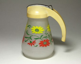 May include: A frosted glass syrup dispenser featuring a pale yellow plastic lid and handle with a thumb-operated metal lever. The body is decorated with a floral pattern of bright yellow and red flowers with green stems and leaves.