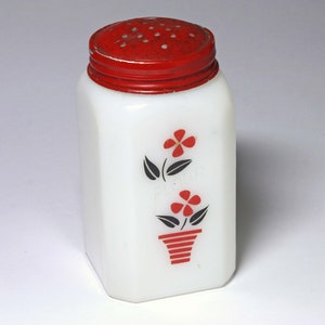 May include: White ceramic salt shaker with a red lid and a floral design. The design features two red flowers with black stems and leaves, one in a red and white striped pot.
