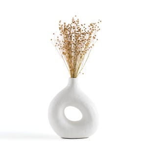 May include: White ceramic vase with a unique, organic shape and a large circular opening. The vase is filled with dried, light brown flowers.