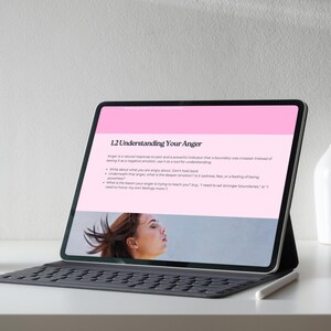 Puede incluir: Una tableta negra con funda de teclado muestra una p&aacute;gina web titulada "1.2 Understanding Your Anger". La p&aacute;gina tiene texto sobre la ira y una foto de una mujer. Un l&aacute;piz &oacute;ptico blanco descansa sobre la mesa.