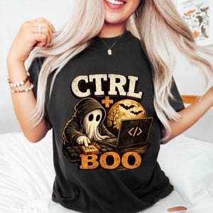 Può includere: Una t-shirt nera con la grafica di un fantasma con felpa con cappuccio che digita su un portatile. Il design include il testo CTRL + BOO, una luna piena, pipistrelli e la sagoma di un albero. Il fantasma preme un tasto con la scritta CTRL.