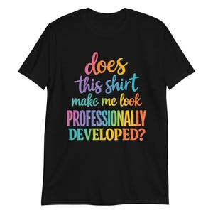 Peut inclure: Un t-shirt noir à manches courtes avec le texte multicolore "does this shirt make me look PROFESSIONALLY DEVELOPED?" imprimé sur le devant. Les lettres utilisent un dégradé de teintes rose, orange, jaune, violet et bleu.