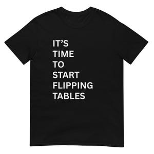 Peut inclure: T-shirt noir avec le texte blanc "IT'S TIME TO START FLIPPING TABLES" disposé verticalement. Le t-shirt a des manches courtes et un col rond.