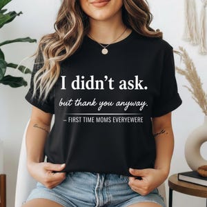 Peut inclure: T-shirt noir avec texte blanc : « I didn't ask. but thank you anyway. » En dessous, « - FIRST TIME MOMS EVERYWHERE ». Le t-shirt est de style col rond.