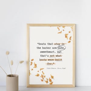 May include: A framed print with a light wood frame. The print features a quote in black text with the word "safe" circled. Decorative orange leaves are scattered around the text. A small vase with dried flowers is on the left.