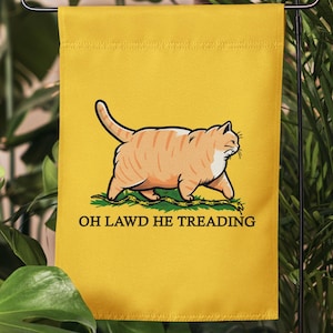 May include: A yellow garden flag with a cartoon orange cat walking on a rope. The text on the flag reads "OH LAWD HE TREADING".
