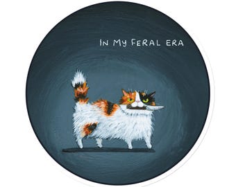 May include: A calico cat with green eyes holds a knife in its mouth. The cat is standing on a dark blue background with the text "In My Feral Era" above it.