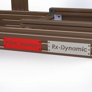 May include: A brown metal frame with horizontal ridges. Two rectangular plates are attached. One is red with the text "K2kc_karaca", and the other is silver with the text "Rx-Dynamic".