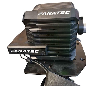 May include: A black Fanatec racing wheel base with a black metal base and a black cable. The wheel base has a silver metal connector and the text "FANATEC" printed on it.