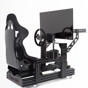 May include: A black racing simulator setup with a bucket seat, steering wheel, and large monitor. The rig is constructed from black metal and includes the text "Dyno ARC". The setup is on wheels.