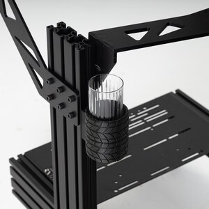 May include: Black metal desk frame with a glass cup holder. The holder is made of black rubber with a tire tread pattern.
