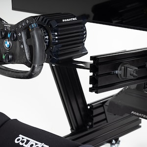 Könnte beinhalten: Ein schwarzer Rennsportsimulator mit Lenkrad, Pedalen und Monitor. Das Lenkrad ist ein Fanatec-Lenkrad mit schwarzem und Kohlefaser-Design. Der Simulator ist aus Metall und hat eine schwarze Oberfläche.