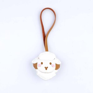 May include: A white leather sheep-shaped keychain with brown ears and a pink blush. The keychain has a brown and tan leather loop for hanging. The sheep has a stitched design and a cute, cartoonish appearance.