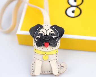 May include: A beige leather pug dog keychain with black ears, nose, and a red tongue. The pug has a yellow collar and a small yellow tag. The keychain is attached to a beige strap. The background is yellow.