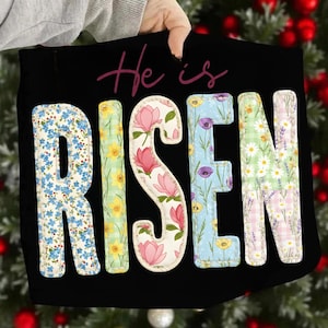 Può includere: Tessuto nero con le parole "He is RISEN" in lettere colorate a motivi floreali. Le lettere sono riempite con motivi di fiori blu, narcisi, magnolie rosa, papaveri viola e margherite. Le parole sono in un carattere decorativo.