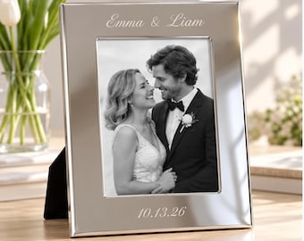 May include: A rectangular silver-toned metal picture frame featuring the engraved names Emma & Liam at the top and the date 10.13.26 at the bottom. The frame holds a black and white photograph of a couple in formal wedding attire.