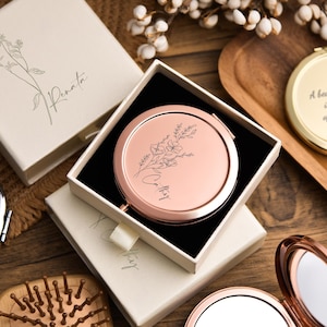 May include: A collection of rose gold compact mirrors, some open and some in their boxes. The mirrors have floral designs and the text "Cathy" and "Renata". One mirror has the text "A beautiful mother is the heart of the family".