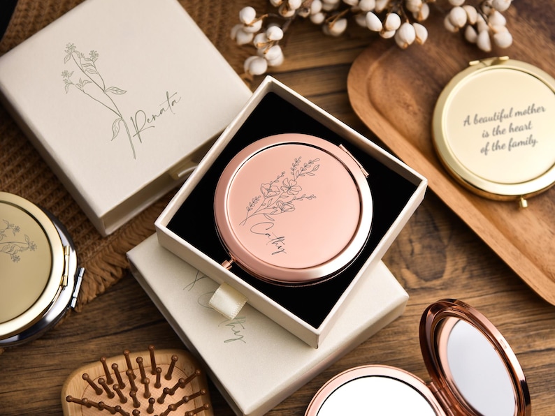May include: A collection of rose gold compact mirrors, some open and some in their boxes. The mirrors have floral designs and the text "Cathy" and "Renata". One mirror has the text "A beautiful mother is the heart of the family".