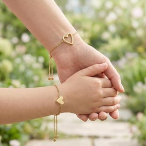 May include: Two gold-toned bracelets featuring heart-shaped charms. One bracelet displays an open-frame heart outline, while the other features a solid, filled-in heart charm. Both pieces are designed with delicate link chains and adjustable sliding clasps.