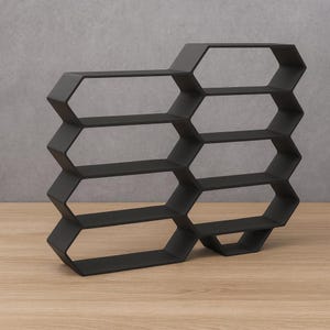 May include: Black honeycomb-shaped wall shelf with multiple shelves. The geometric design features a series of interconnected hexagonal shapes, creating a modern and stylish storage solution. The shelf is made of a solid material and is suitable for displaying books, decor, or other items.