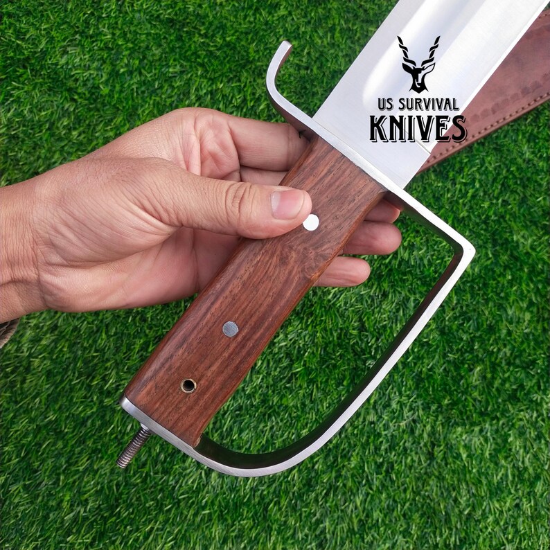 Pode incluir: Uma faca de sobreviv&ecirc;ncia grande com uma l&acirc;mina de a&ccedil;o polido e um cabo de madeira escura. O cabo &eacute; fixado com rebites de metal. A faca tem uma guarda distinta e o texto "US SURVIVAL KNIVES" &eacute; vis&iacute;vel na l&acirc;mina.